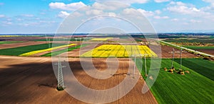 Aerial shot of transmission towers electricity pylons with power lines in cultivated agricultural field, drone pov