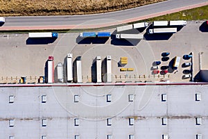 Aerial Shot of Truck with Attached Semi Trailer Leaving Industrial Warehouse/ Storage Building/ Loading Area where Many Trucks Are