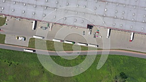Aerial Shot of Truck with Attached Semi Trailer Leaving Industrial Warehouse/ Storage Building/ Loading Area where Many Trucks Are