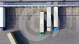 Aerial Shot of Truck with Attached Semi Trailer Leaving Industrial Warehouse Storage Building Loading Area where Many Trucks Are