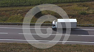 Aerial shot of truck with cargo trailer driving on empty straight road. Flying over white lorry moving along highway