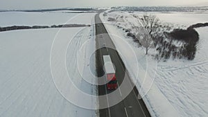 Aerial shot of truck and cars driving winter road in snowy field.