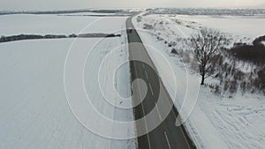 Aerial shot of truck and cars driving winter road in snowy field.