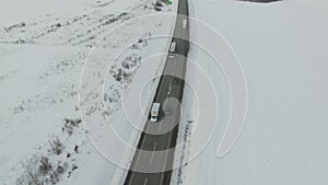 Aerial shot of vehicle and bus driving winter road in snowy field.