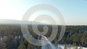 Aerial shot of winter road with lonely approaching car. Background snowy north forest