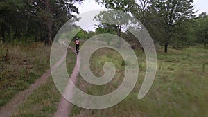 Aerial shot of young sportiveman rides bicycle on forest road at summer evening. Healthy cycling lifestyle