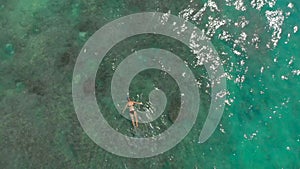 Aerial shot of a young woman snorkeling in an open sea watching corals and exotic fishes