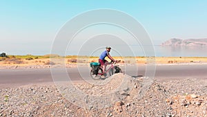 Aerial side tracking view young fit caucasian male cyclist cycle fully loaded bicycle tour bike by scenic lake background in sunny