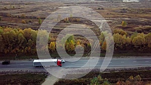 Aerial side view of flat-nosed truck moving along a highway with cargo trailer.