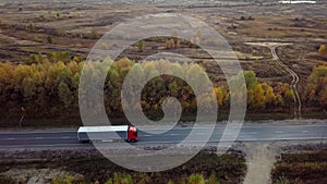 Aerial side view of flat-nosed truck moving along a highway with cargo trailer.