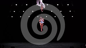 Aerial silk duo with white costume on black stage background performing at high altitude