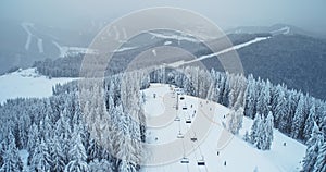 Aerial skier in winter going down ski lift from mountain. Forest in white snow, slow motion.