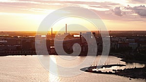 Aerial slide and pan shot of production or logistic halls in industrial neighborhood. View against golden sunset