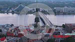 Aerial slide and pan shot of tall and slim tower of St. Peters Church, wide river and modern buildings on opposite bank