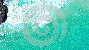 Aerial sliding shot over bodyboarders and waves in clear tropical blue water