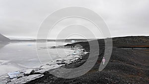 Aerial slow motion view tourist woman traveler walk by Fjallsjokull glacier in Iceland outdoors while travels