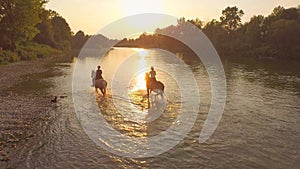 AERIAL: Small black dog watching the two women horseback riding at sunset.