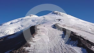 Aerial of snowy mountain peak on blue sky background. Clip. High rock top covered by white snow, natural scenery of