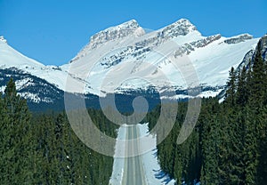 AERIAL: Spectacular view of snowy Canadian Rockies towering above empty road.