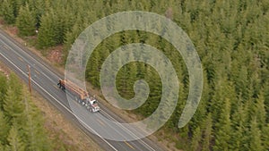 AERIAL: Speeding big rig transports heavy logs down an empty asphalt highway.