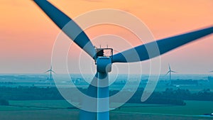 Aerial straight of back of wind turbine with distant turbines in green farmland at sunset