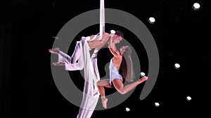 Aerial straps duo with white costume on black stage background doing performance