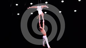 Aerial straps duo with white costume on black stage background performing and flying high