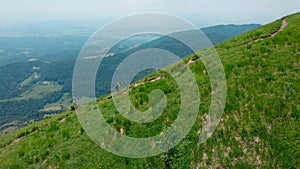 AERIAL: Stunning view of young female trekking up mountain trail with her dog