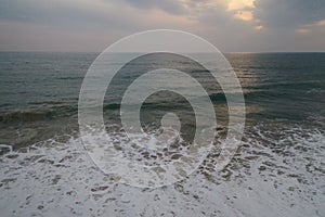 Aerial sunset drone bird view shot of the sea surface with turquoise blue water, large white waves and foam forming beautiful