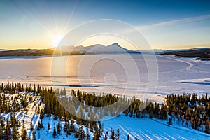 AERIAL: Sunset golden light over Norwegian snowy winter mountains and Rossvatnet lake, pine and birch trees, early spring, calm