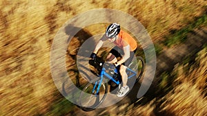 Aerial telephoto lens tracking shot of an athletic man riding fast along rye field pathway