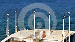 Aerial telephoto parallax of wind generators on a building rooftop with blue ocean water in background