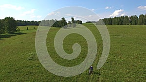 AERIAL: Three kids cycling on bicycles through green field.