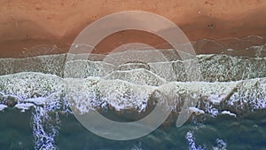 Aerial top down shot of sand beach on a summer day while turquiose sea waves breaking on sandy coastline.