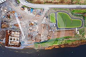 Aerial top down view on a construction site of a bridge by a river with tall white crane. Development and city structure concept