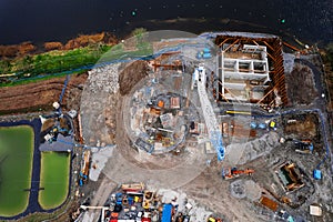 Aerial top down view on a construction site of a bridge by a river with tall white crane. Development and city structure concept