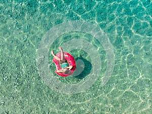 Aerial top down view of cute young girl floating on toy ring at Myrtos beach, the most beautiful beach of Kefalonia, a large coast