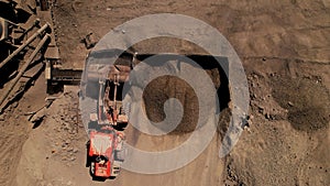 Aerial top down view of an excavator loading crushed stone into a dump truck in a crushed stone quarry. Conveyor and