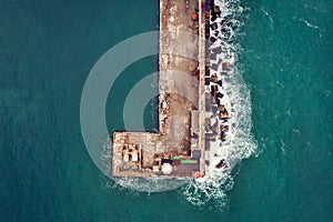 Aerial top down view of old concrete pier or breakwater with lighthouse and emerald sea water with waves