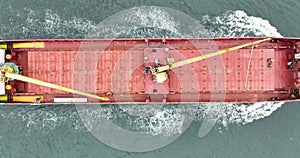 Aerial top down view of a red cargo ship sailing in open sea.