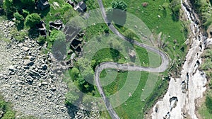 Aerial: top down view tailspin over winding mountain road on the Italian Alps, crossing green meadow and pasture in alpine valley,