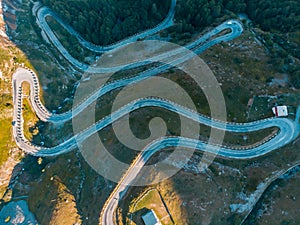 Aerial: top down view tailspin over winding mountain road on the Italian Alps, crossing green meadow and pasture in alpine valley,