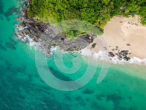 Aerial top down view of tropical beach with turquoise water, white sand and big rock. Trees and palms growing on the rock.