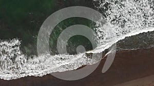 Aerial top down view of waves splashing on sand coastline at sunny day. Drone goes along seashore. Nature travel summer