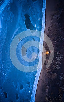 Aerial top view from above of lonesome car at frozen sea coastline with headlights on. Lonely road trip traveller enjoys