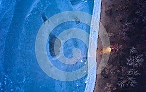 Aerial top view from above of lonesome car at frozen sea coastline with headlights on. Lonely road trip traveller enjoys