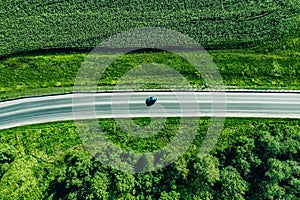 Aerial top view of a asphalt road with a car through .green forest and corn field