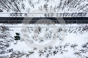 Aerial top view. asphalt road through winter snow-covered landscape with bare trees