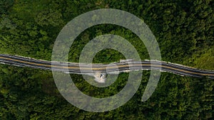 Aerial top view of asphalt roads in the forest and small tourist car parked on side of the road