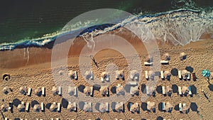 Aerial top view on the beach. Umbrellas, sand and sea waves. Summer holidays.